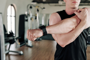 Fototapeta na wymiar Sportsman wearing smart watch when stretching arms when warming up in gym