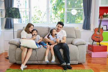 full shot happy Asian family, father, mother daughter and son singing karaoke on the sofa in the...