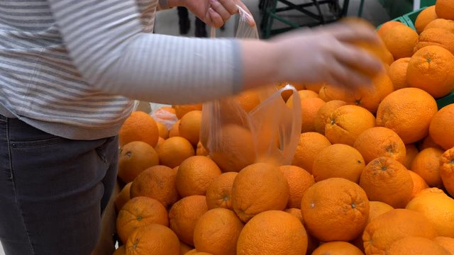 close-up hands of adult woman picking orange in supermarket and puts fruits on knitted mesh made of eco-friendly materials. selective focus