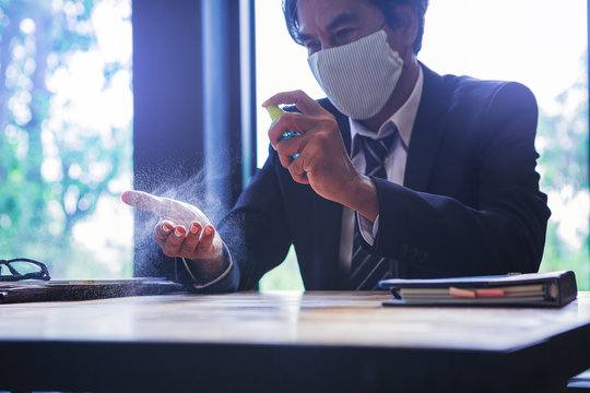 Businessman with mask applying alcohol spray for cleaning and protecting hands from virus disease