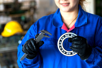 Femal technician hand holding ball bearing and vernier caliper tools..