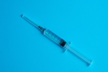 Medical syringe with vaccine on a blue background. Top view