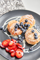 Cottage cheese pancakes or syrniki with blueberry and strawberries on black plate, closeup view. Condensed milk sauce. Russian, Ukrainian cuisine. Healthy tasty breakfast