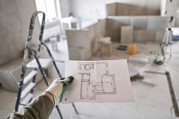 The construction worker hold in hands Architectural blueprints. Repair or construction of a new apartment. Concept for new house design or home improvement. Development of the apartment project.