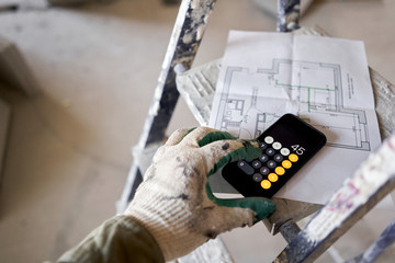 The construction worker calculates the area of the room on the calculator. Architectural...