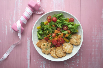close up of salad and tuna fish on plate with dumbbell on table 