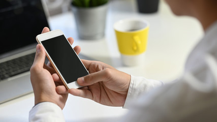 Cropped image of business people's hands holding a smartphone while sitting in front computer laptop, coffee cup that putting on working table in comfortable office. Orderly workplace concept.