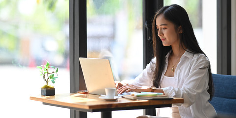 Side shot of young beautiful woman in white shirt typing on computer laptop while sitting at the...