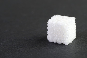 Side view of a sugar cube on a gray background. Sugar cube close-up on the right of the frame. Cube sugar texture. Side view, close-up, horizontal, free space on the left. Health and nutrition concept