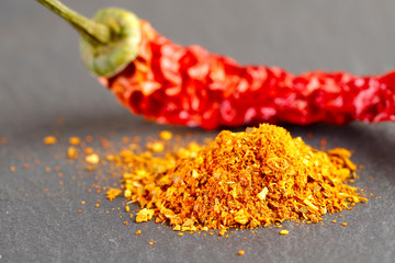 Food background. Blurred image of a pod of dry red hot pepper. In the foreground a bunch of orange ground spices on a gray textured surface. Side view, horizontal, free space. Food concept.