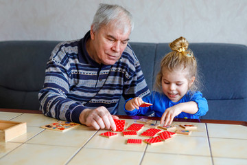 Beautiful toddler girl and grandfather playing together pictures memory table cards game at home....