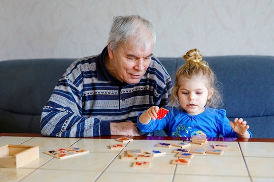 Beautiful toddler girl and grandfather playing together pictures memory table cards game at home. Cute child and senior man having fun together. Happy family indoors