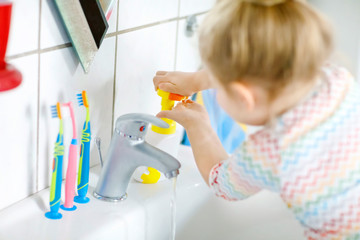 Cute little toddler girl washing hands with soap and water in bathroom. Adorable child learning...