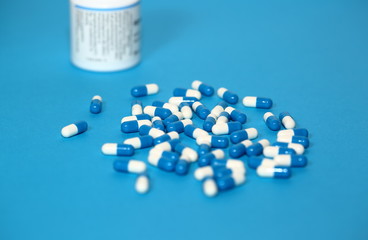 Capsules tablets pills on blue background close up and pharmaceutical bottle in soft focus