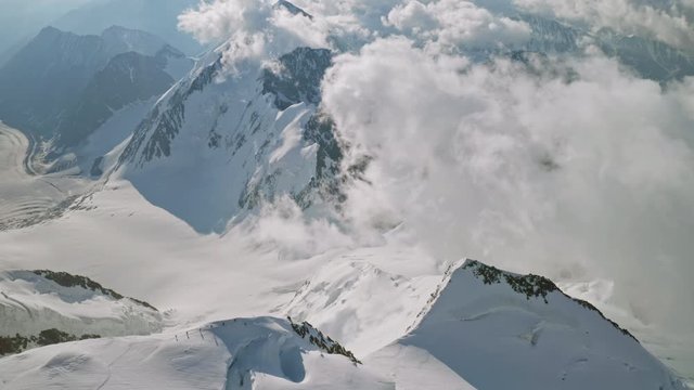 Magic alpine panorama, alpinists climbs on snow scarp, clouds float below summit