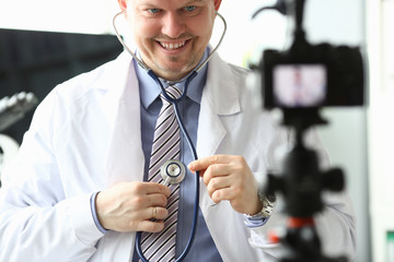 Smiling doctor shows to listen lungs stethoscope. Young doctor is trying to make information available to viewers. Man eats examples from his life. Funny stories related to medicine