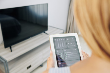Woman using application on tablet computer when changing channels and setting volume on tv set