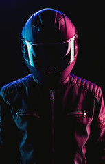 A guy in a motorcycle helmet and leather jacket against a background of neon lights and smoke - obrazy, fototapety, plakaty