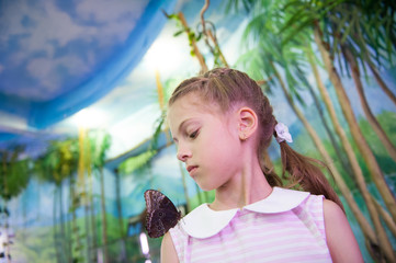 educational process of interested little girl looking at butterfly insect sitting on her shoulder...