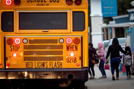 School Bus With Flashing Lights And Children Boarding Diffused In The Distance