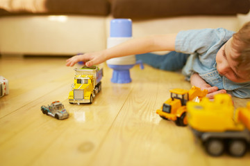 Little boy playing with toy car truck on wooden floor. 