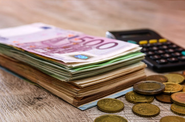 Euro banknotes with calculator and coins on a wooden background. Close-up. Business concept.
