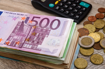 Euro banknotes with calculator and coins on a wooden background. Close-up. Business concept.