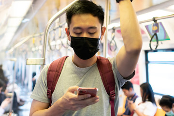 Close up of one young Asian man wearing black surgical face mask and using mobile phone in subway train during Coronavirus Covid-19 pneumonia outbreak and pm 2.5 smog air pollution crisis in big city.