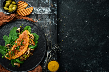 Omelet with mushrooms and spinach in a black plate. Top view. Free space for your text.