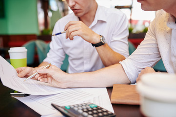 Serious young entrepreneurs reading contract or agreement at meeting and discussing details and corrections