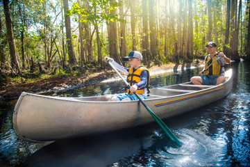 Adventuresome Father and son canoeing together on a beautiful river in a thick forest. Family vacations and new experiences. Smiling and having fun together in nature