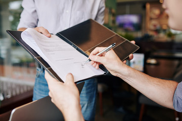 Close-up image of businessman signing contract in hands of his business partner