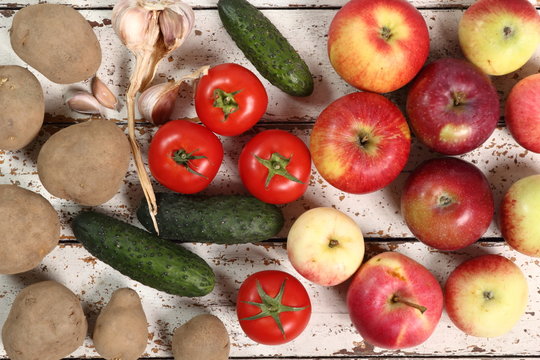 Tomatoes, Cucumbers, Potatoes, Garlic and Apples on peeled paint plank background. Directly Above.