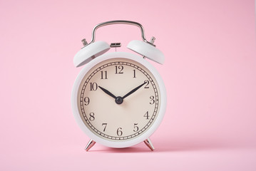 White retro alarm clock on the pink background with copy space. Time concept