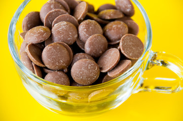 Drops of milk chocolate in a transparent Cup on a yellow background