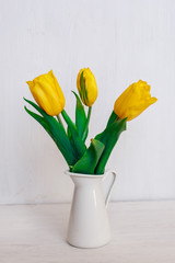 bouquet of yellow tulips in a white vase on a white wooden background