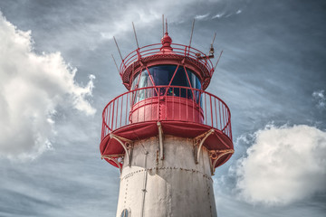 Historic red lighthouse on background of blue dramatic sky.
