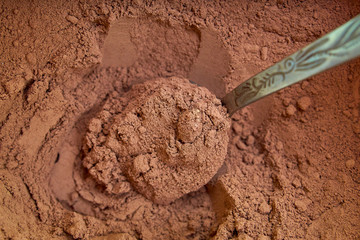 Cocoa powder in a spoon on cocoa powder background. Close-up.
