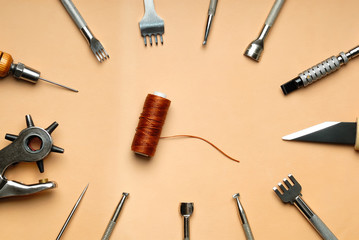 Leather crafting DIY tools lies on natural beige leather.