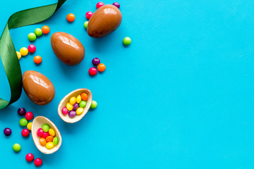 Easter background with chocolate eggs and dragees on blue background top-down frame copy space