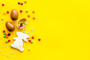 Easter sweets frame. Chocolate eggs and bunny gingerbread on yellow background top-down frame copy space