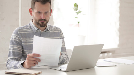 The Casual Young Man Doing Paperwork and Typing on Laptop