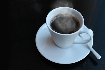 Top view of black coffee in a white cup with saucers and  spoons on a black background. There are smoke floating on top.  You can placed copy AD. on it .