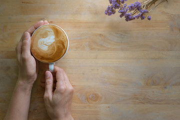 Woman's hands holding a cup of coffee on wooden table.
