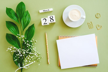 Wooden cubes calendar March 28. Notepad, cup of coffee, bouquet flowers on green background. Concept hello spring Top view Flat lay Mock up