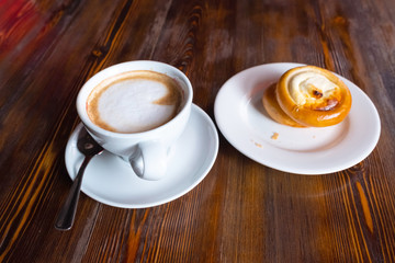 cup with cappuccino and saucer with a bun view from a high point