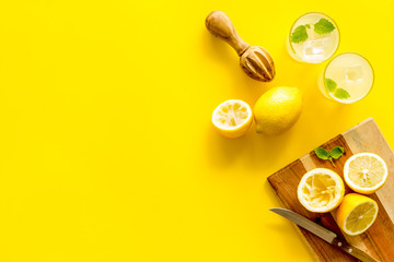 Homemade lemonade in glasses near juicer and cut lemons on yellow background top-down copy space