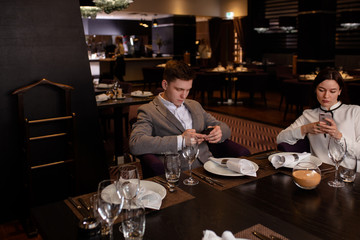 caucasian couple use mobile phone in restaurant. guy and lady came to have dinner together, but both of them busy with their work in mobile phones