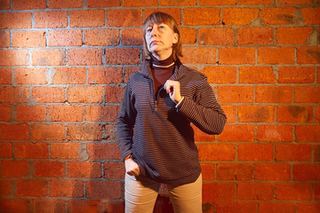 A middle-aged woman poses showing clothes near red brick wall. An inept model in an inept shoot