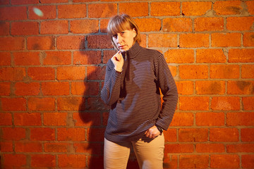 A middle-aged woman poses showing clothes near red brick wall. An inept model in an inept shoot